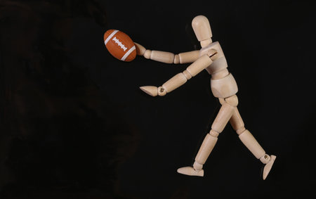 Wooden puppet mannequin playing with rugby ball isolated on black backgroundの写真素材