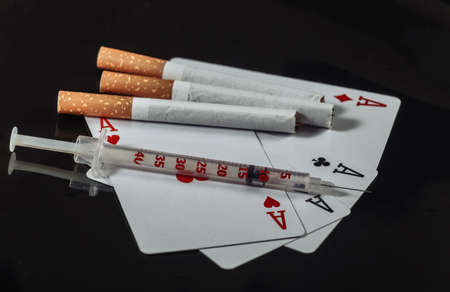 Cigarette and syringe, four aces isolated on black background. Nicotine, gambling and drug addictionの写真素材