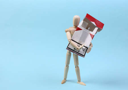 A wooden puppet holds a pack of cigarettes on a blue background. Nicotine addictionの写真素材