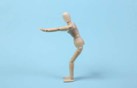 Wooden puppet practices squats against blue background. Aerobic conceptの写真素材