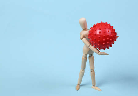 Wooden puppet holding a covid-19 virus strain molecule on a blue backgroundの写真素材