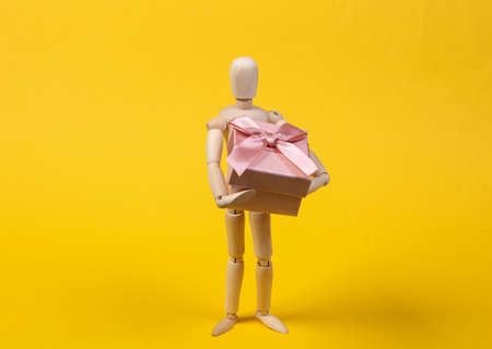 Wooden puppet holding gift box isolated on yellow backgroundの写真素材