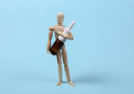 A wooden puppet holds nasal spray on a blue background. medicine conceptの写真素材