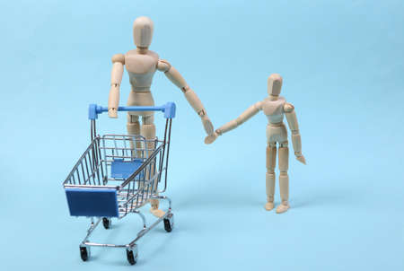 shopping concept. Wooden puppets with supermarket trolley on blue background. Spending time togetherの写真素材