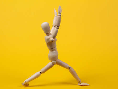 Wooden puppet practicing yoga asana pose on yellow backgroundの写真素材