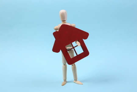 Wooden puppet holds figure of house on blue background.の写真素材