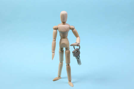 Wooden puppet holds keys on blue background.