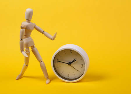 Wooden puppet and clock on yellow background.の写真素材