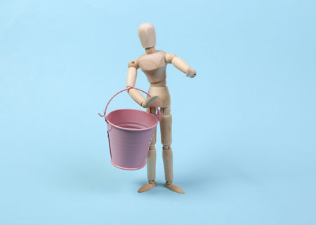 Wooden puppet holding bucket on a blue background.の写真素材