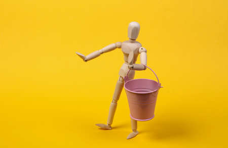 Wooden puppet holding bucket on yellow background.の写真素材