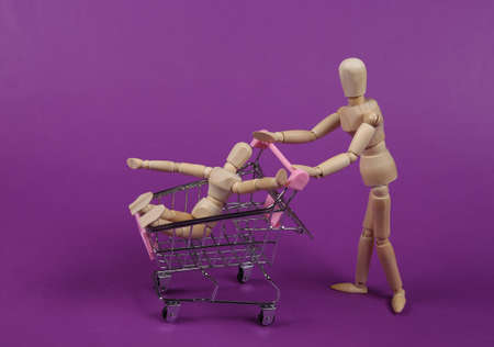 Two wooden puppets with supermarket trolley shopping together on purple backgroundの写真素材