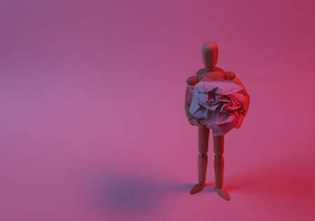 Wooden puppet holding crumpled paper balls in red neon light.