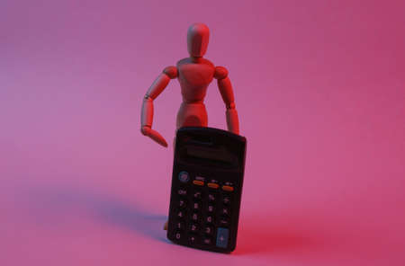 Wooden puppet is pointing at calculator in red neon light. Cost calculation, economics