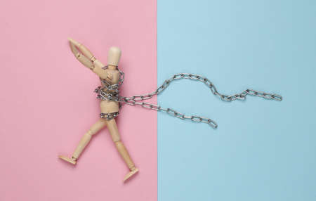 Wooden puppet wrapped in a steel chain runs on a blue-pink background. top viewの写真素材