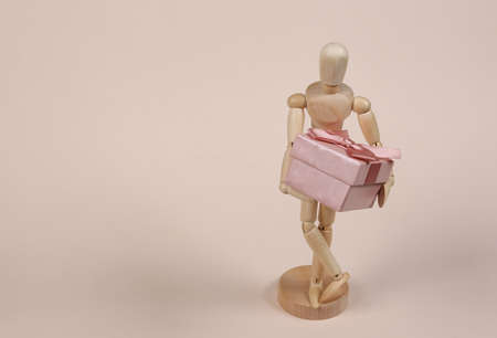 Wooden puppet mannequin holding a gift box on beige background.の写真素材