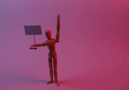 Protesting activist wooden puppet with blank banner in neon red light. meeting. Defending your...