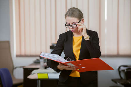 Business lady carefully examines documents in folder in officeの写真素材