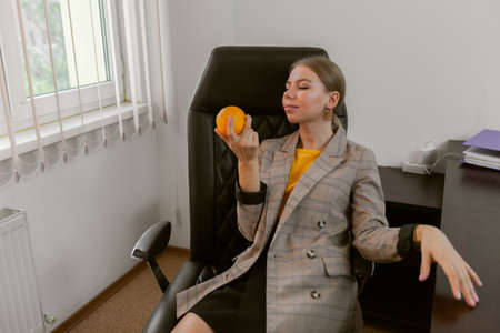 Business lady holding an orange while sitting at the table in her office