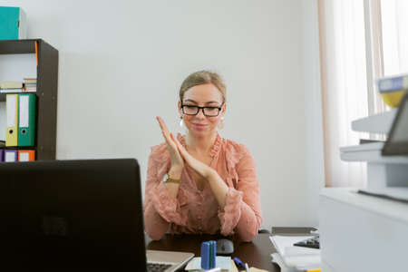 Confident cheerful office worker woman rubbing hands while sitting at workspace in officeの写真素材