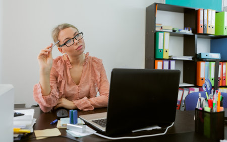Pensive young business woman seated at her workplace in the office. office worker, business conceptの写真素材
