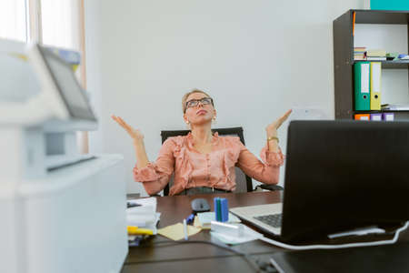 Perplexed business woman looking up while sitting at table in officeの写真素材