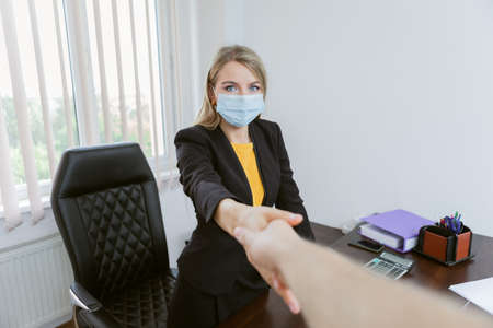 You're hired! Lady boss in madicine mask shakes hands in her officeの写真素材