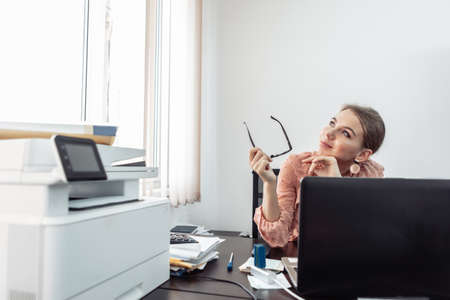 Pensive, dreaming woman office worker at her workplaceの写真素材