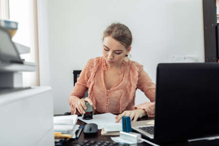 Young business woman puts a stamp on a document in her workplaceの写真素材