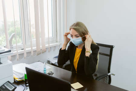Business lady puts on a medical mask on her face in the office.の写真素材