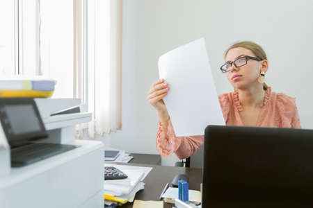 Attentive woman secretary carefully looks into document at her workplaceの写真素材
