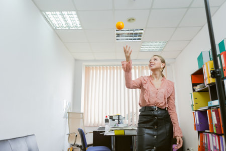 Business woman tossing an orange on the background of the workspace in the officeの写真素材