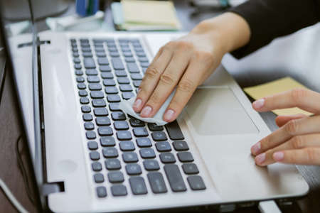 Business woman wipes laptop keyboard with damp cloth in officeの写真素材