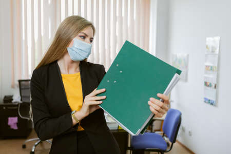 business woman in medical mask holding folder in officeの写真素材