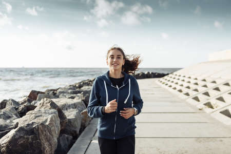 Young curly haired woman runner running along the urban embankmentの写真素材