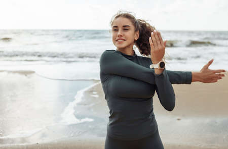 Curly sports woman in sportswear doing body warming up or stretching exercise on beach. healthy lifestyleの写真素材