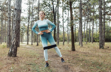 Young fitness woman with curly hair working out with fitness rubber bands in the forest