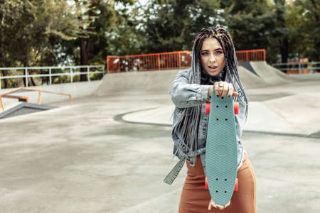 Extraordinary female millennial skater with colorful makeup, African braids in a skate park. Youth, lifestyle conceptの写真素材