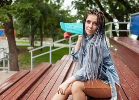 Extraordinary woman skater with afro-braids, skateboard sits on the podium.