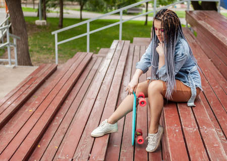 Extraordinary woman skater with afro-braids, skateboard sits on the podium.の写真素材