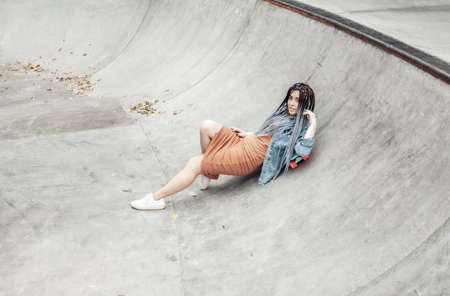 Cheerful extraordinary millennial woman with bright makeup and African lies on penny board in a skateparkの写真素材