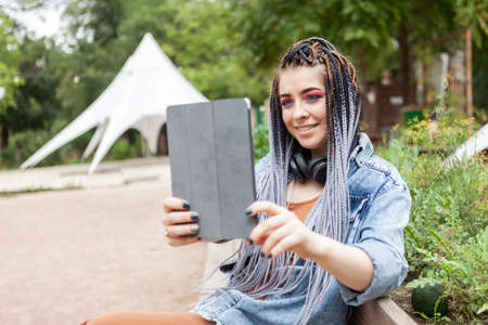 Extraordinary woman student millennial with african pigtails using tablet outdoors