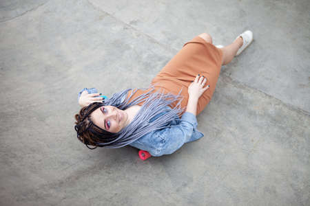 Cheerful extraordinary millennial woman with bright makeup and African lies on penny board in a skateparkの写真素材