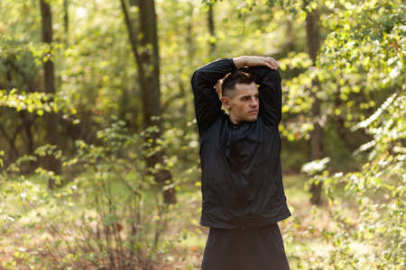 Active sport man trains warm-up exercises or stretching in the autumn forest. healthy lifestyle. outdoor workoutの写真素材