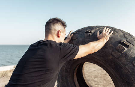 Active fitness man lifts heavy wheels on an outdoor training ground. cross-training. healthy lifestyleの写真素材