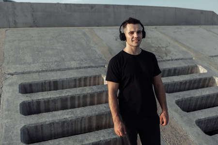 Active muscular sports man listening to music in stereo headphones outdoors on concrete slabs backgroundの写真素材