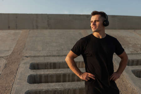 Active muscular sports man listening to music in stereo headphones outdoors on concrete slabs backgroundの写真素材