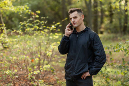 Handsome man talking on the phone in autumn forestの写真素材
