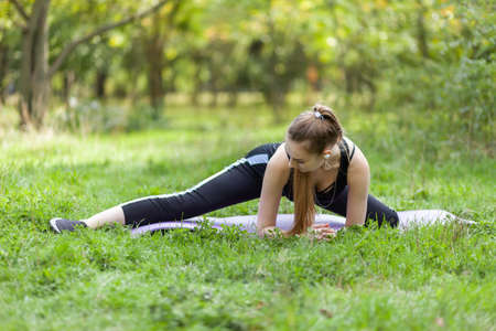 Active fit woman in sportswear is practicing stretching exercise in the park on a bright sunny day....