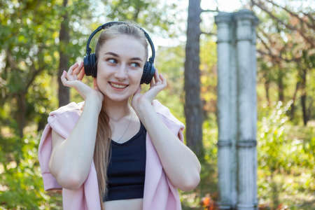 Healthy cheerful fit woman listening to music in stereo headphones in the park