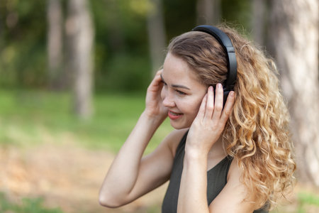 Attractive active yogi woman with curly hair listens to relaxing music with headphones in the forest